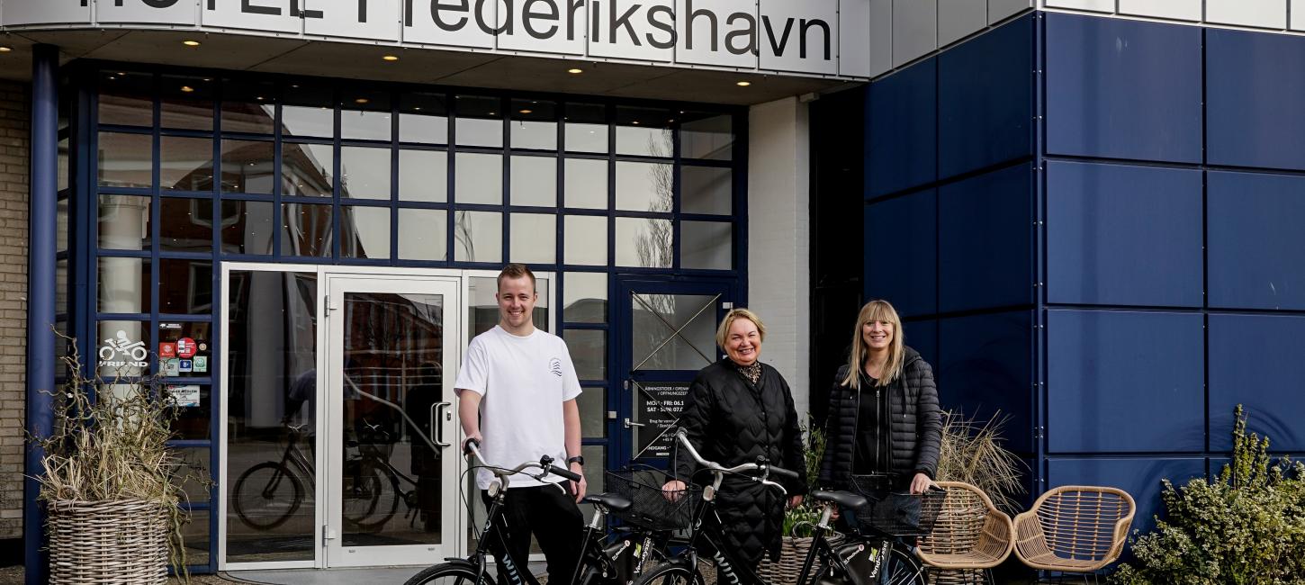 Tre mennesker der står med cykler foran Hotel Frederikshavn